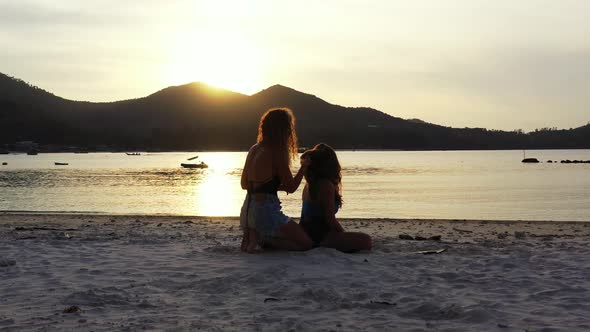 Happy young women playing with curly hair on exotic beach washed by calm lagoon reflecting beautiful