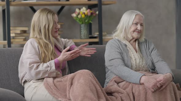 Middle Aged Caucasian Woman Arguing with Senior Lady Sitting on Couch Indoors