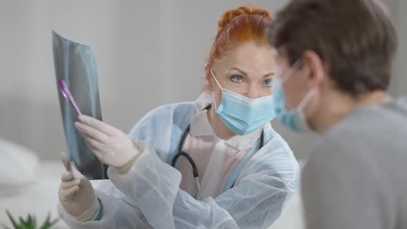 Portrait of Focused Caucasian Woman in Covid Face Mask Pointing at Lungs Xray Talking to Blurred Man