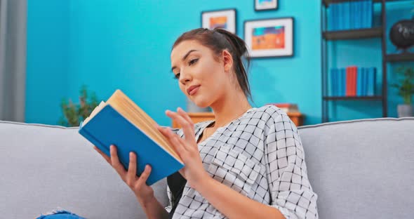 Pretty Female with Hair Pinned Up Relaxes in Homely Attire While Delving Into Book That