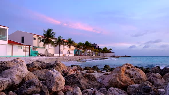 Beach houses with palmtrees next to tropical rocky coast during sunset