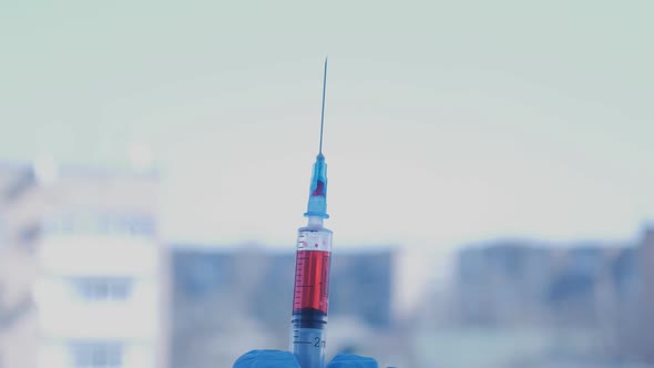 Shooting of Syringe Needle with Drop of Blood on the Background Windows in the City