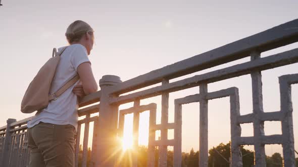 A Woman Stands at the Railing of the Bridge, Looking Into the Distance