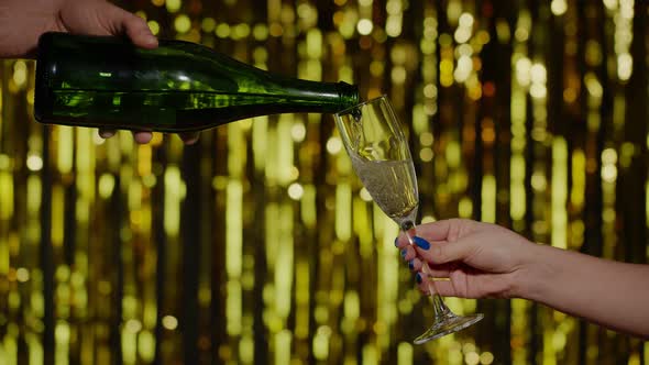 Champagne Alcoholic Drink Is Poured From Bottle Into Drinking Glasson Gold Background in Slow Motion