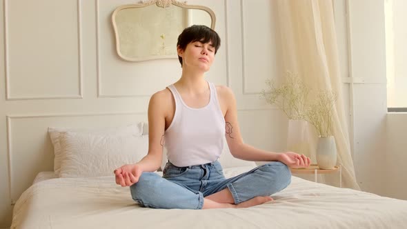 Young woman meditating while sitting on the bed at home in bedroom.