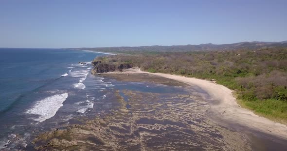 Aerial drone view of the beach, rocks and tide pools in Playa Palada, Guiones, Nosara, Costa Rica.