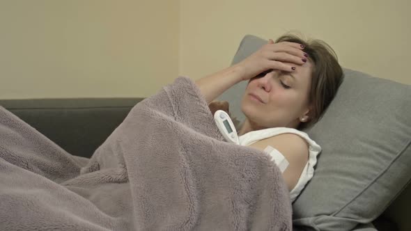 Young Woman Lies on the Sofa Wrapped in a Plaid