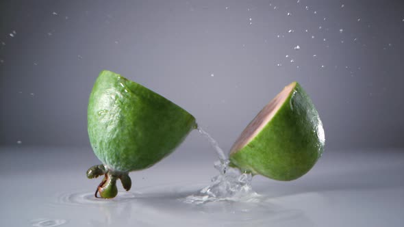 Halved feijoa fruits falling on water surface. Slow Motion.