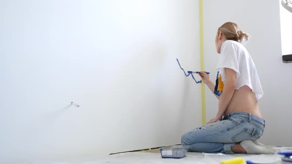woman paints with blue paint on the wall of a room