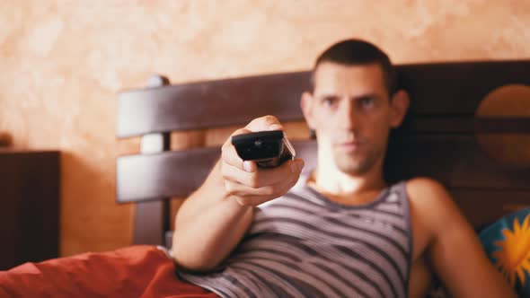 Tired Man Lies on the Bed and Emotionally Watches TV with Remote Control