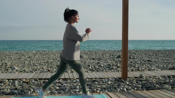 Young Sporty Woman Is Training Outdoors Near Empty Sea Coast, Squatting