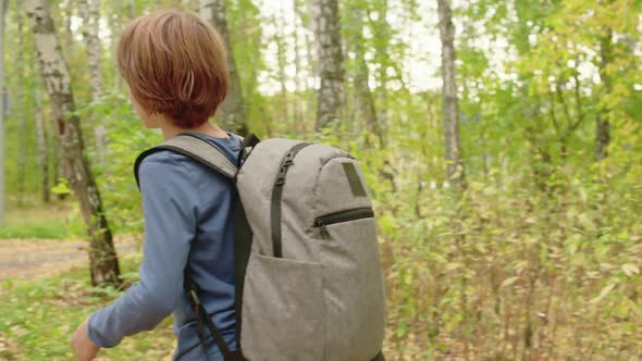 Rear View Teenager Boy with Backpack Walking on Pathway in Autumn Park