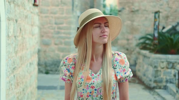 Elegant Woman in Summer Hat Walking Down the Old Street