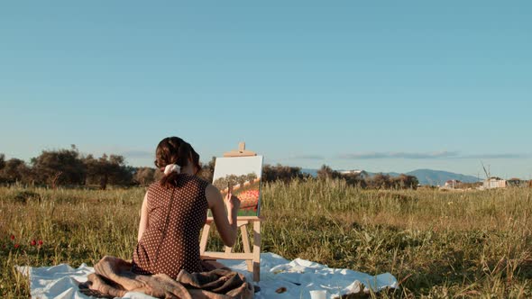 Young girl paints the picture on canvas in the countryside