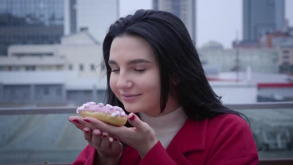 Close-up Portrait of Young Smiling Caucasian Woman Smelling Donut and Looking at Camera. Cheerful