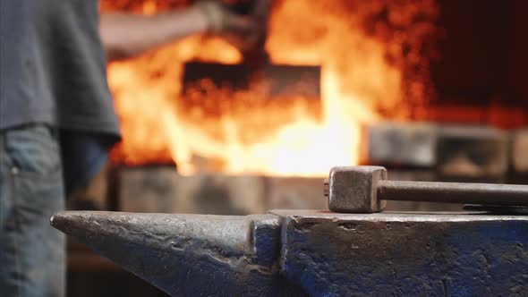 Hammer on Anvil in Forge on Fire Background in Which Worker Throws Garbage.