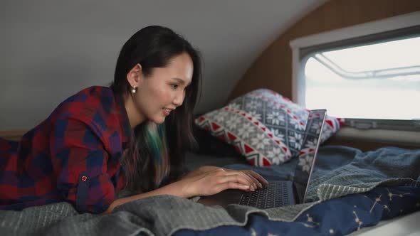 Asian Woman Freelancer Working at a Laptop While Lying in a Mobile Home Typing Text Remote Work in