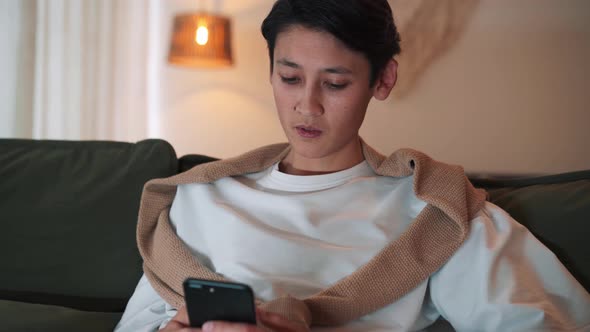 Concentrated Asian man texting by phone and looking TV