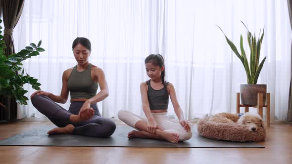 Mom and little daughter doing yoga Sukhasana or Lotus pose together mat at home