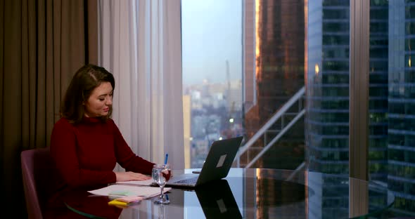 A Woman Sits in the Office of a Business Center at a Table, in Front of Her Is a Laptop, a Glass
