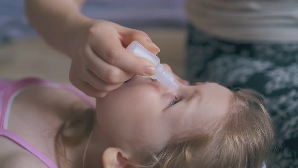 Mommy Gives Eye Drops To Crying Girl on Soft Bed Closeup