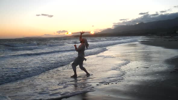 A man fire dancer and performer in silhouette spinning his flaming staff in the ocean water on the b