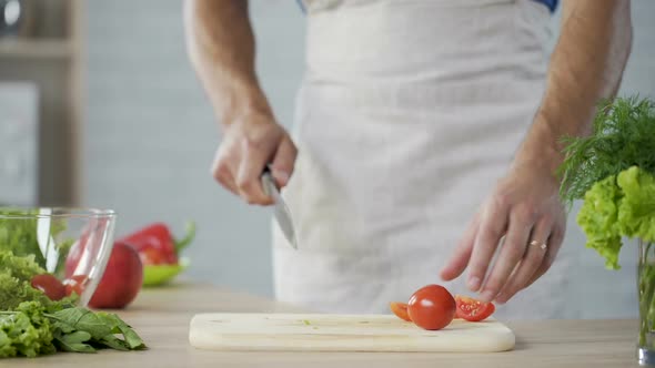 Man in Apron Carefully Cutting Tomatoes for Salad and Putting Them in Bowl