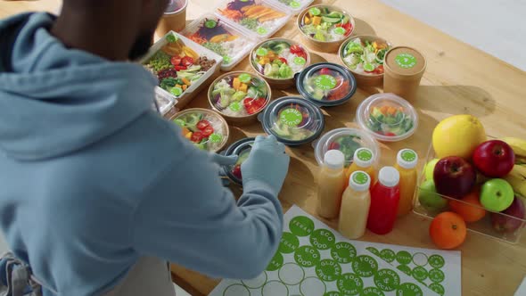 Black Male Worker Applying Stickers on Containers with Healthy Meals