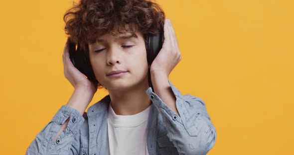Close Up Studio Portrait of Curly Little Boy Enjoying Music in Big Wireless Headphones