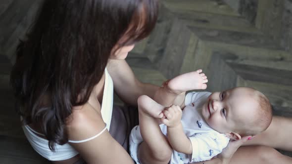 Happy Young Mother Talking Playing with Her Infant Baby Child on Floor in Room
