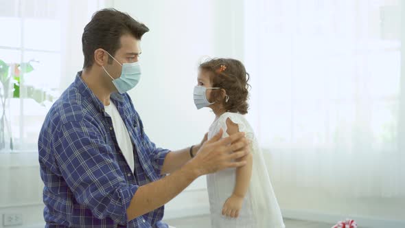 Father is wearing the face mask and pouring alcohol hand wash gel to his little daughter to protect 