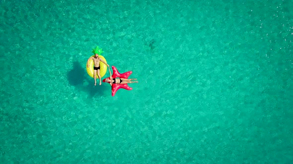 Aerial view of man and woman floating on inflatable mattresses holding hands.
