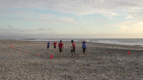 A group of guys playing flag football on the beach.