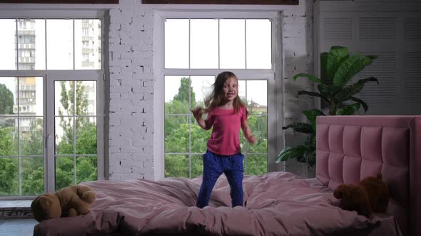 Happy Little Child Jumping on Cozy Bed in Bedroom alt