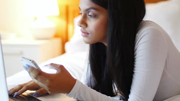 Woman using a laptop and mobile phone in bedroom