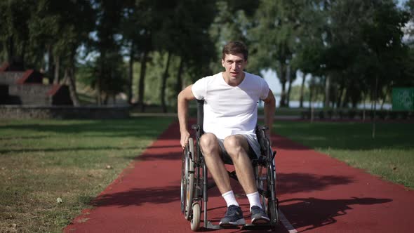 Smiling Man Rolling Wheelchair on Sports Field on Sunny Spring Summer Day