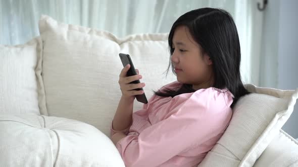 Beautiful Asian Girl Playing Smartphone  Sitting On A Sofa In The Living Room At Home