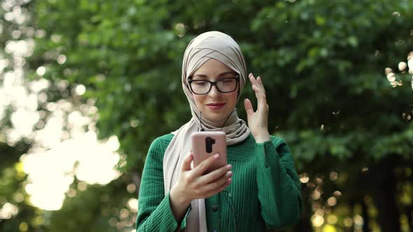 Young Muslim Woman Listening to Music While Walking Down a City Park