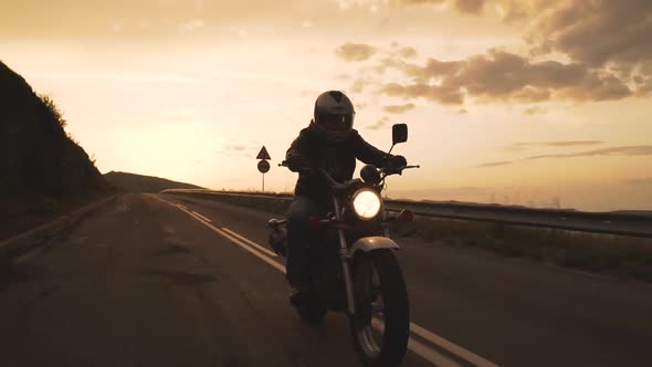 Silhouette of Biker Riding Vintage Motorcycle on Country Road at Sunset