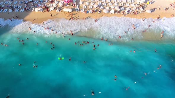 People Swim on Light Blue Sea in the White Sandy Beach Near the Rocky Mountainside