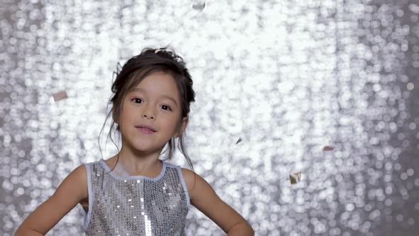 Cute Happy Little Girl Child in a Silver Dress Dancing on Background of Silver Bokeh