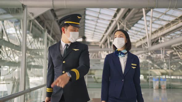 Airliner pilot and air hostess wearing face mask walking in airport terminal to the airplanel.