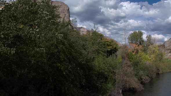 Flying over river and trees towards rocky cliff face