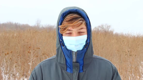 a Young Caucasian Teenager Man Dressed in Warm Winter Clothes Stands on the Street in a Blue Medical