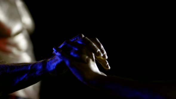 Two Hands with Metallic Golden Skin Touch Palms Interlace Fingers on a Black Background