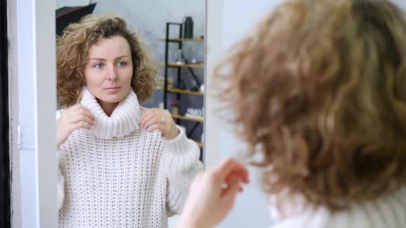 Young Woman Wearing Knitted Sweater Standing In Front Of The Mirror At Home