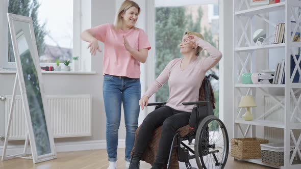 Wide Shot of Cheerful Young Woman Dancing with Handicapped Friend Indoors