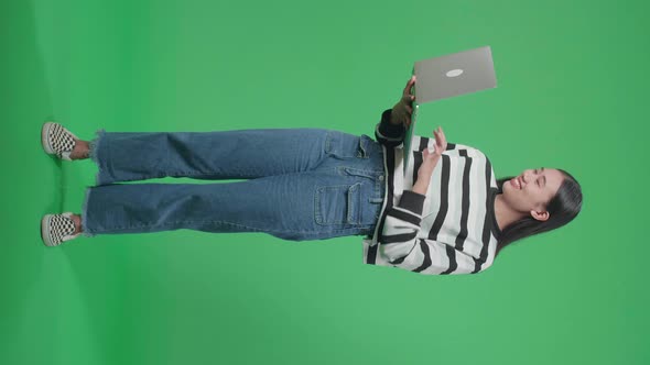 Full Body Of A Smiling Asian Woman Typing On Computer While Standing In Front Of Green Screen