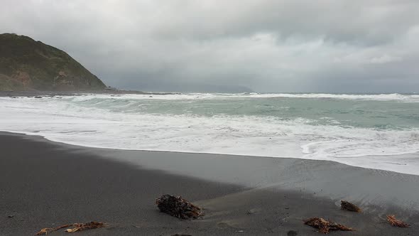 Large rolling waves on remote and rugged black sand coastline beach on a bleak, grey and overcast da