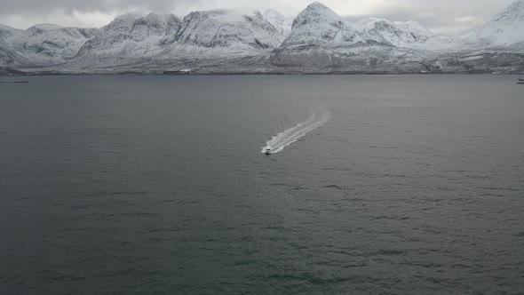 Epic aerial pan of racing speedboat in Arctic waters, snow-covered mountains behind